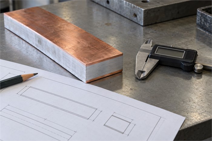 CCA busbar sample beside an engineering drawing and a digital caliper on a workbench.